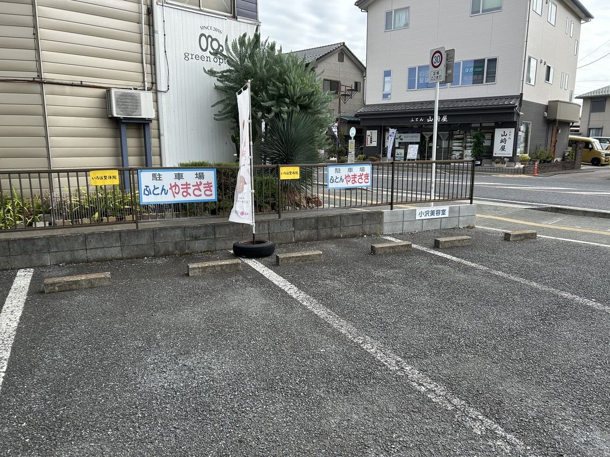 駐車場②。道路を渡った斜め向かいのスペース。「駐車場 ふとんやまざき」の看板が目印で、道路の向こう側に店舗が見えます。